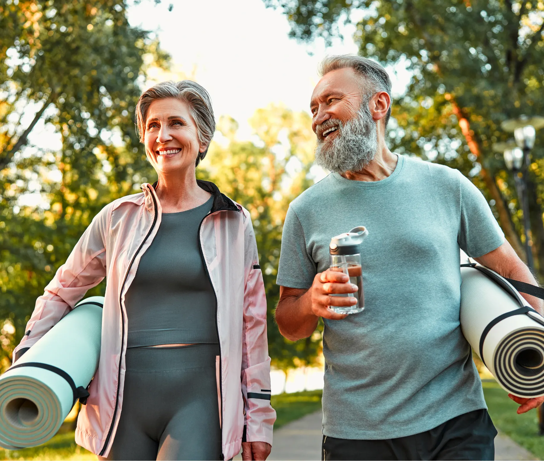 Man and woman outdoors with yoga mats under arms