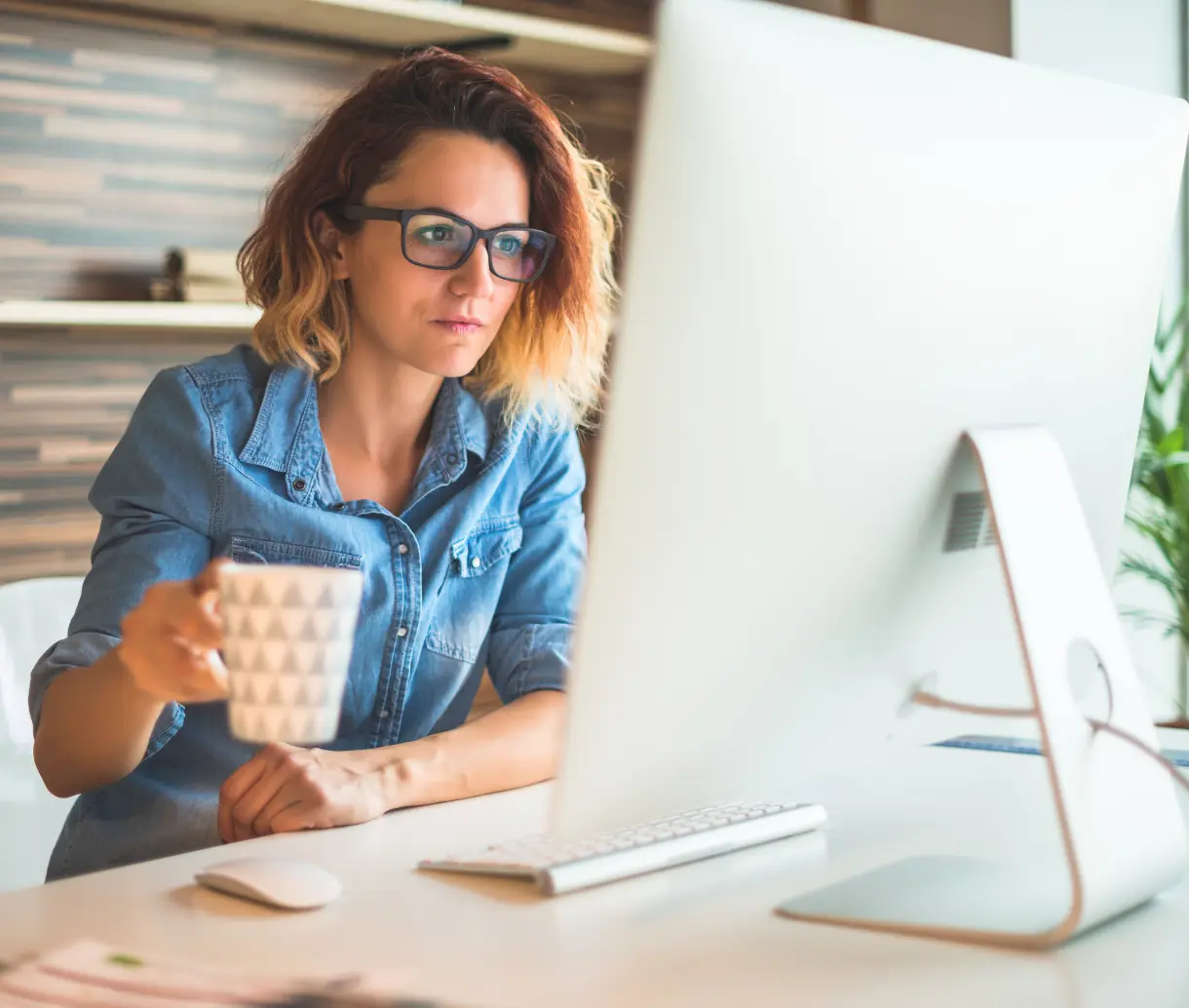 Woman holding coffee sitting at computer